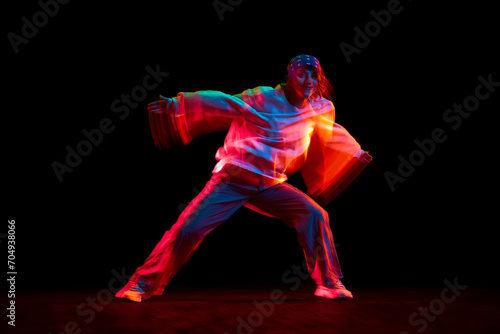 Young woman in casual clothes dancing hip hop isolated over black background in neon light with mixed lights effect. Concept of contemporary dance, street style, youth, hobby, action, lifestyle
