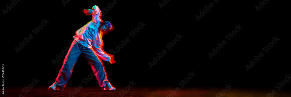 Fototapeta premium Young girl, hip hop dancer in motion, dancing isolated over black background in neon light. Concept of contemporary dance, street style, youth, hobby, lifestyle. Banner. Empty space to insert text