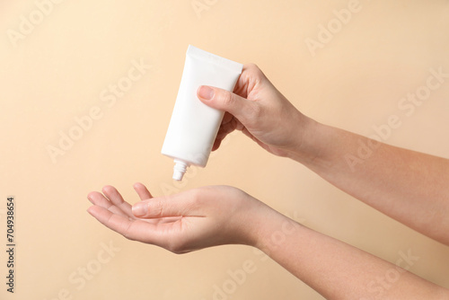 Woman applying cosmetic cream from tube onto her hand on beige background, closeup