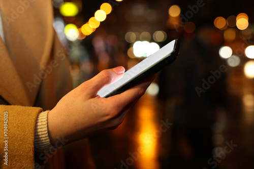 Woman with smartphone on night city street, closeup. Space for text