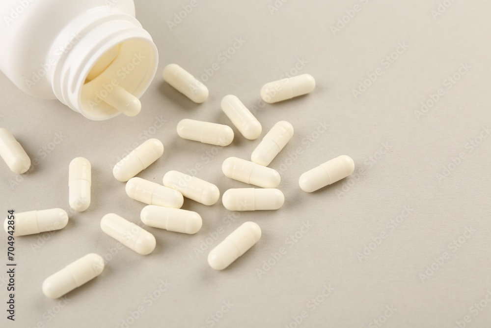 Bottle and vitamin capsules on light background, closeup. Space for text