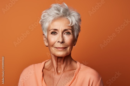 Portrait of smiling senior woman on orange background. Looking at camera.