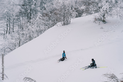 Snowboarder kneels near a skier sitting in the snow on a mountain slope