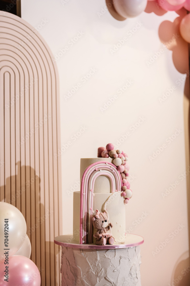 Arch decorated with pink, brown balloons. Cake is decorated bear figure, rainbow. Trendy baptism cake for girl. Delicious reception at a birthday party. Photo wall decoration space or place for text.