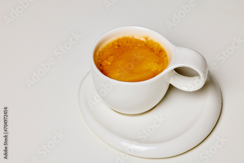 a white cup with coffee on a plate.