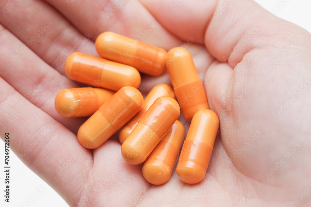 Female hand holding pills. Woman open hand with medicine. Drugs isolated on white background. Orange vitamin capsules on girl hand. Cutout hand holding diet supplement. Female hand holding pills. Woman open hand with medicine. Drugs isolated on white background. Orange vitamin capsules on girl hand. Cutout hand holding diet supplement.