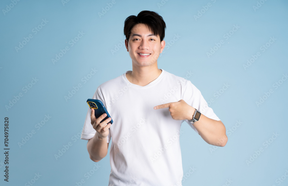 Fototapeta premium Portrait of Asian guy using phone and posing on blue background