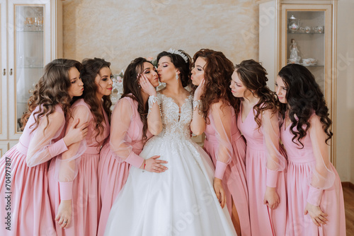 Portrait of the bride with her friends in the room. A brunette bride in a long white dress and her friends in pink dresses are smiling and happy. Young girls.