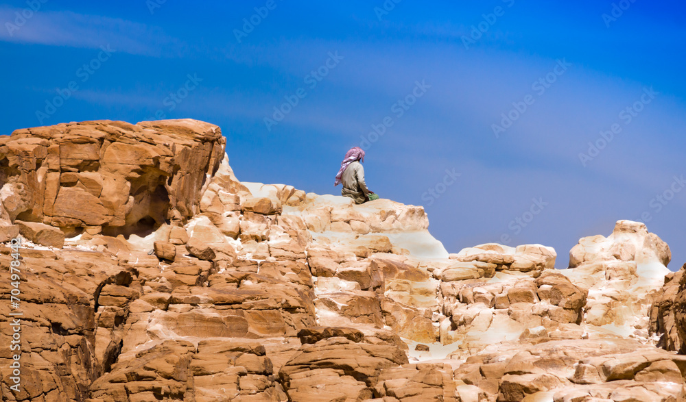 Bedouin sitting on the peak of a high stone rock against a blue sky in Egypt Dahab South Sinai