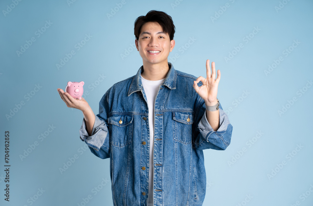 Portrait of an Asian guy holding a piggy bank and posing on a blue background Portrait of an Asian guy holding a piggy bank and posing on a blue background