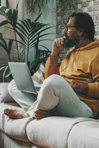 Canvas Print Mature man sitting at home with crossed legs and working on laptop