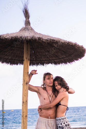 Young couple ij love at the beach in summer holiday vacation leisure activity together - hug and relationship people with blue ocean and sky in background - travel and happy lifestyle man and woman