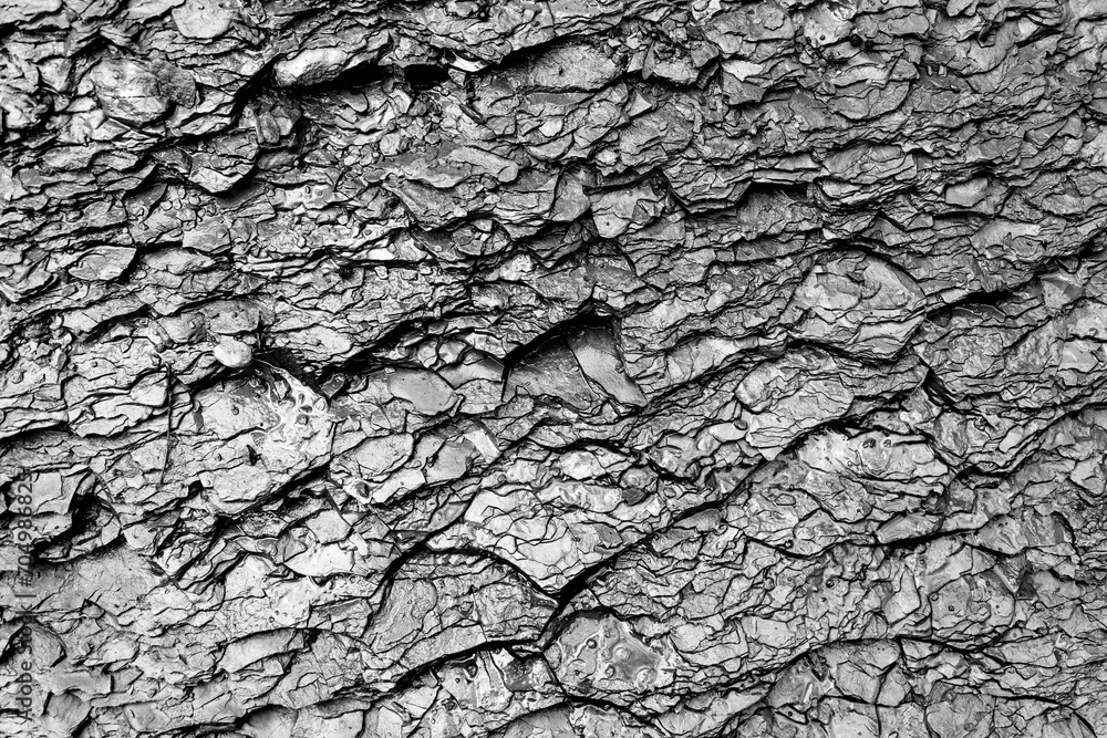 Slate rock background with dark contrasting stone layers, cracks caused by erosion. Wet rough surface near a waterfall in Germany. Fine-grained, foliated geologic formation. Black and white greyscale. Slate rock background with dark contrasting stone layers, cracks caused by erosion. Wet rough surface near a waterfall in Germany. Fine-grained, foliated geologic formation. Black and white greyscale.