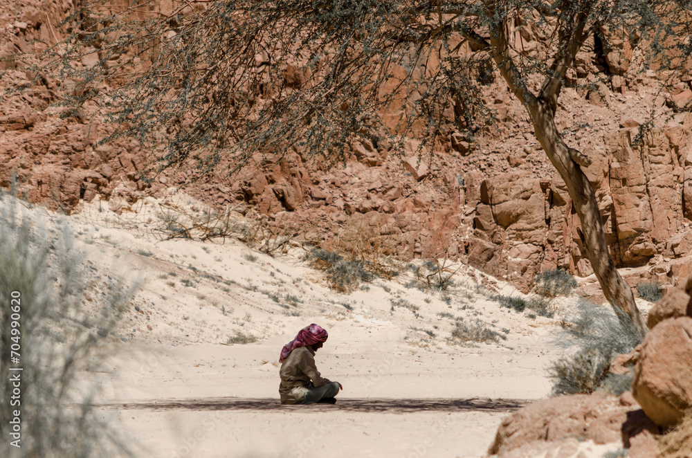 Bedouin prays sitting on the sand in the shade of a tree in the desert against the backdrop of mountains in Egypt Dahab South Sinai