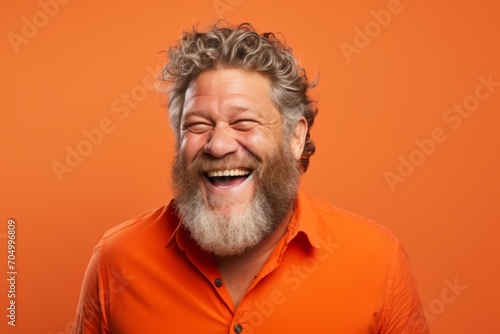 Portrait of a happy senior man with long gray beard and mustache laughing on orange background © Inigo