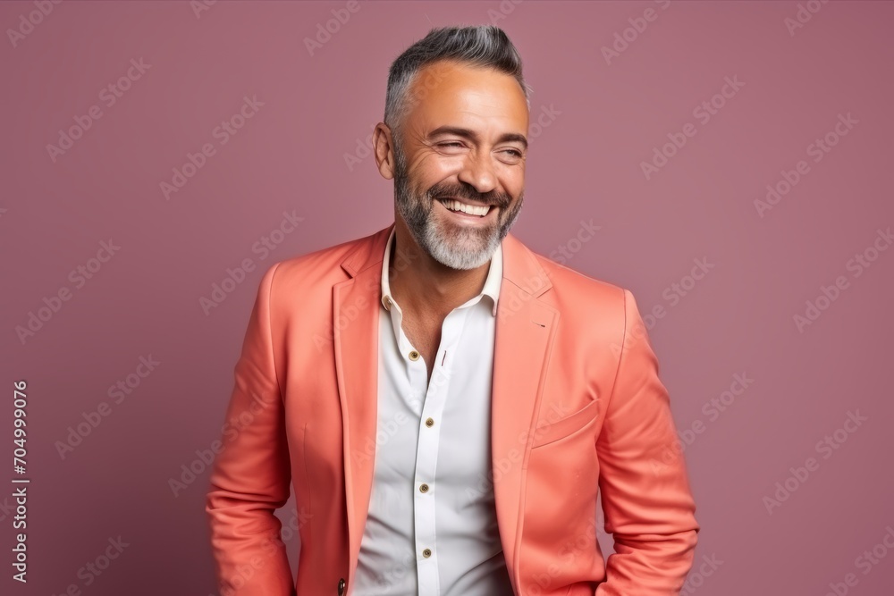 Portrait of a handsome mature man in an orange jacket smiling at the camera while standing against a purple background