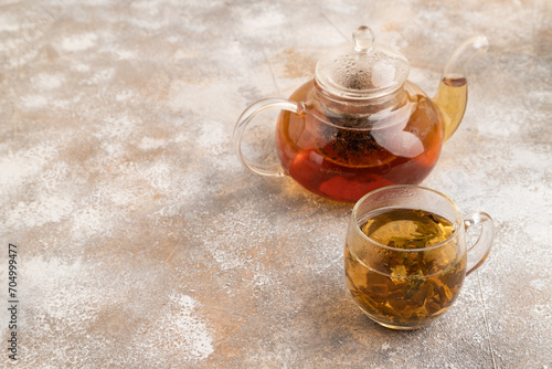 Red tea with herbs in glass teapot on brown concrete. Side view, copy space.