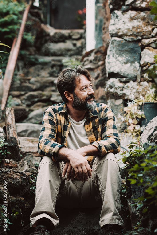 Hipster outdoor mature bearded man sitting on a rocks stairs and enjoying nature around looking and resting - single male people lifestyle concept - relax and feeling with nature - adult man sit down 