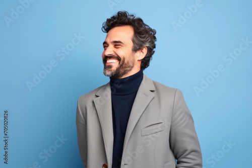 Handsome man with coat laughing and looking to the side on blue background