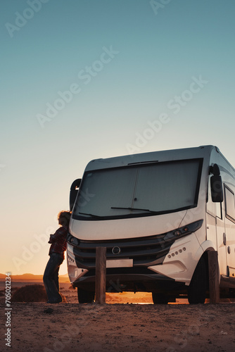 People and camper camping car van freedom concept lifestyle or alternative transport vacation. Big van parked off road and woman resting outside. Colorful sunset and sky with golden mountains 