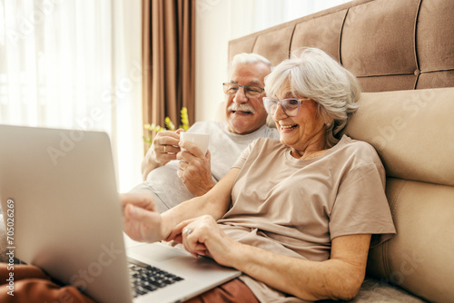 A happy senior couple using laptop in bed in the morning.