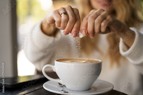 Close-up of female hands pours sugar into coffee. Adding sweetener or fructose to beverage. Daily drink, unhealthy food
