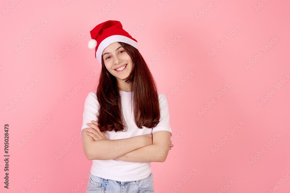 Smiling teenage girl with Santa hat with crossed arms on pink background in studio. Smiling teenage girl with Santa hat with crossed arms on pink background in studio.