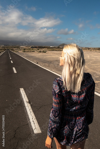 Blonde long hair girl viewed fromback walk on a long straight asphalt road - concept of freedom and independence - hope and future for next destination in life photo