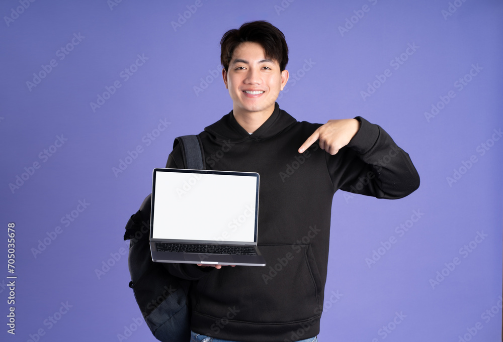 Asian male student using laptop on purple background Asian male student using laptop on purple background