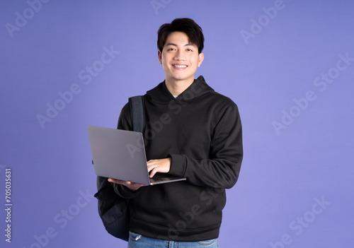 Asian male student using laptop on purple background