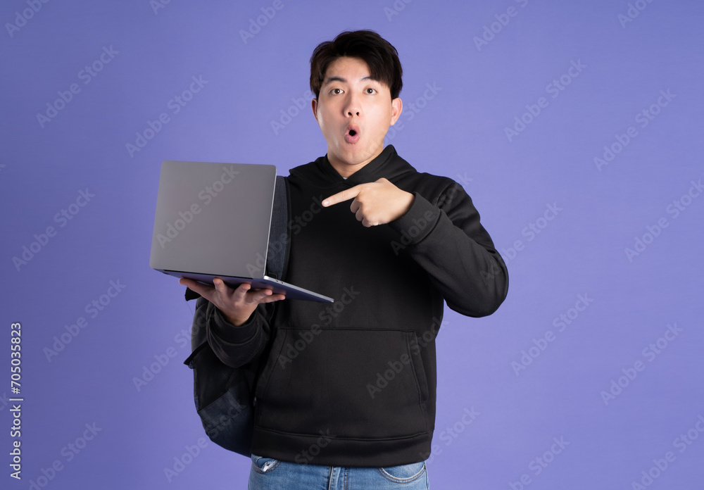 Asian male student using laptop on purple background Asian male student using laptop on purple background