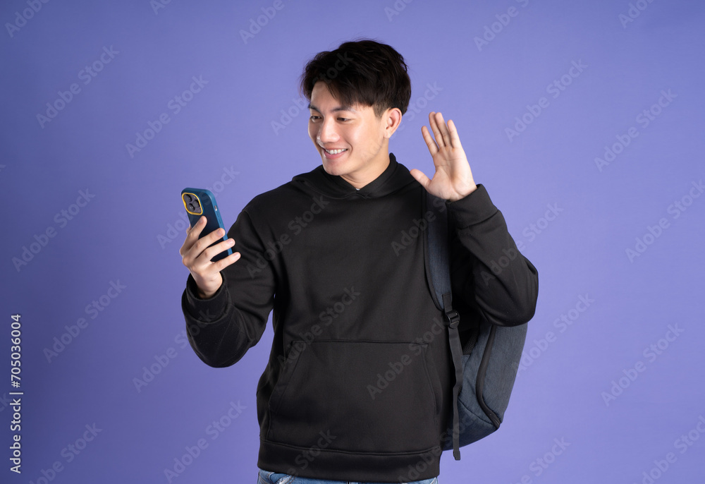 Asian male student using phone on purple background Asian male student using phone on purple background