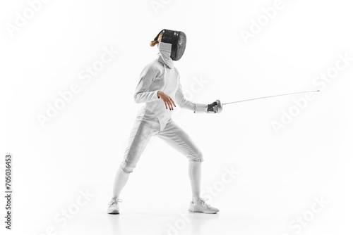 Female athlete in fencing gear showcasing her impeccable form, sword poised for action against white studio background. Confidence and strength. Concept of professional sport, active lifestyle. Ad
