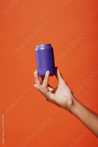 cropped shot of person holding purple soda can in hand on orange background, carbonated drink