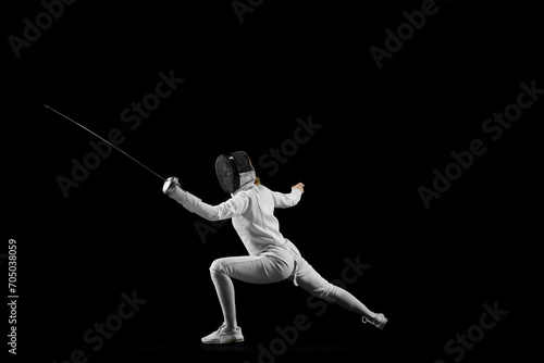 Fencer's footwork and poised stance in mid-bout against pristine black studio background. Tactical aspect dynamic sport. Concept of professional sport, active and healthy lifestyle, championship. Ad