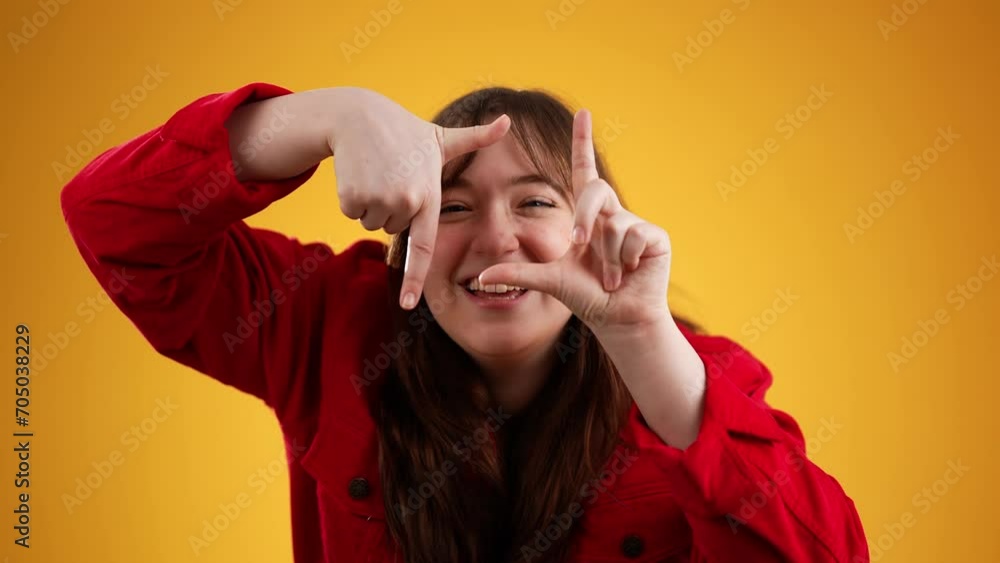 Portrait of woman looking at camera through tinger frame isolated on yellow background with copy space Portrait of woman looking at camera through tinger frame isolated on yellow background with copy space