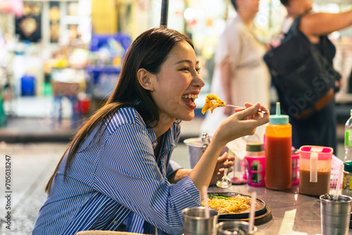 Young Asian woman traveler tourist eating Thai street food in China town night market in Bangkok in Thailand - people traveling enjoying food culture concept photo