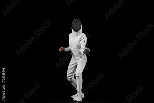 Energy portrait of female fencer lunges forward, her blade poised to strike against black studio background. Concept of professional sport, active and healthy lifestyle, championship. Ad