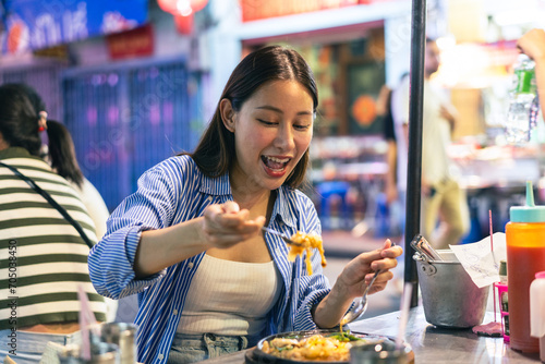 Young Asian woman traveler tourist eating Thai street food in China town night market in Bangkok in Thailand - people traveling enjoying food culture concept