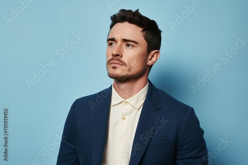 Portrait of a pensive young businessman looking away while standing against blue background