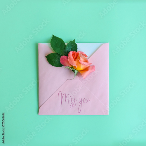 Romantic layout made of pink envelope, gradient pink and orange rose flower and MISS YOU message against pastel mint green background. Woman's day. Valentine design.
