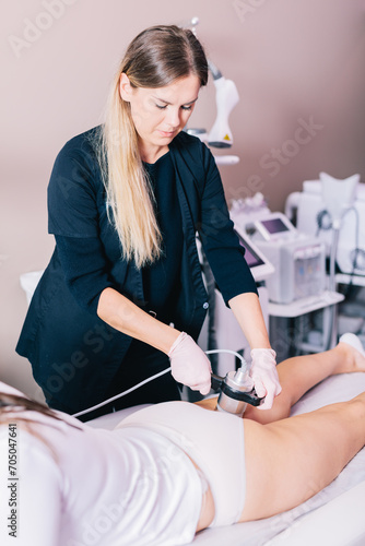 Fotografie Woman, a beautician doing radiofrequency RF treatment on her client's thigh in a beauty salon