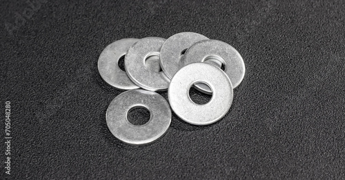 Metal washers neatly arranged on a matte black surface. Metal washers for bolts and screws. The subdued backdrop, emphasizing the precision of the metal washers.