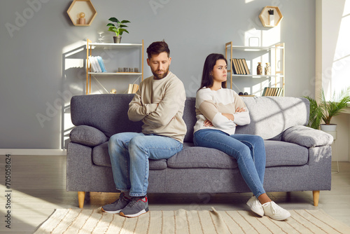 Family couple ignoring each other after a quarrel. Two people turn away and don't talk to each other. Angry young man and woman sitting back to back, with arms crossed on the sofa in the living room photo