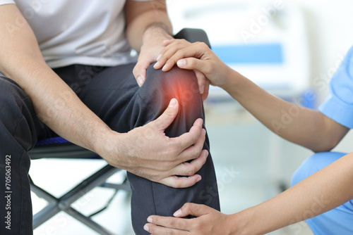 Female doctor diagnosing knee pain of male patient in wheelchair in hospital examination room. photo