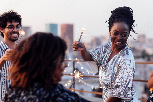 Glamorous African girls in elegant dresses and mixed-race smiling man drink champagne