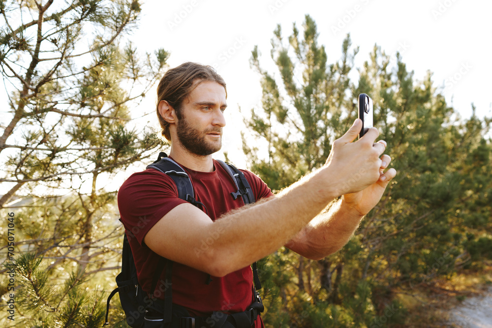 Hiker man with backpack checks the route on his phone on the walking trail Hiker man with backpack checks the route on his phone on the walking trail