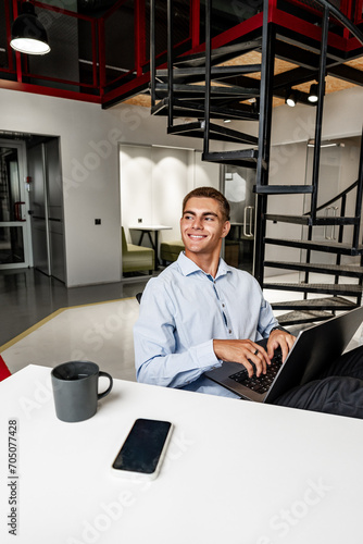 Smiling young businessman relaxing on chair with his feet resting on table