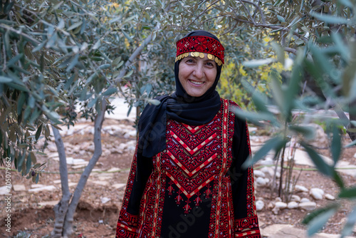Portrait Of woman wearing palestinian traditional clothes in olive trees field holding branch in her hand photo