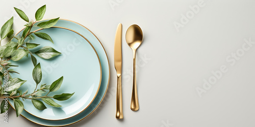 Golden cutlery arranged neatly on a white plate with a blue rim, adorned with green leaves photo